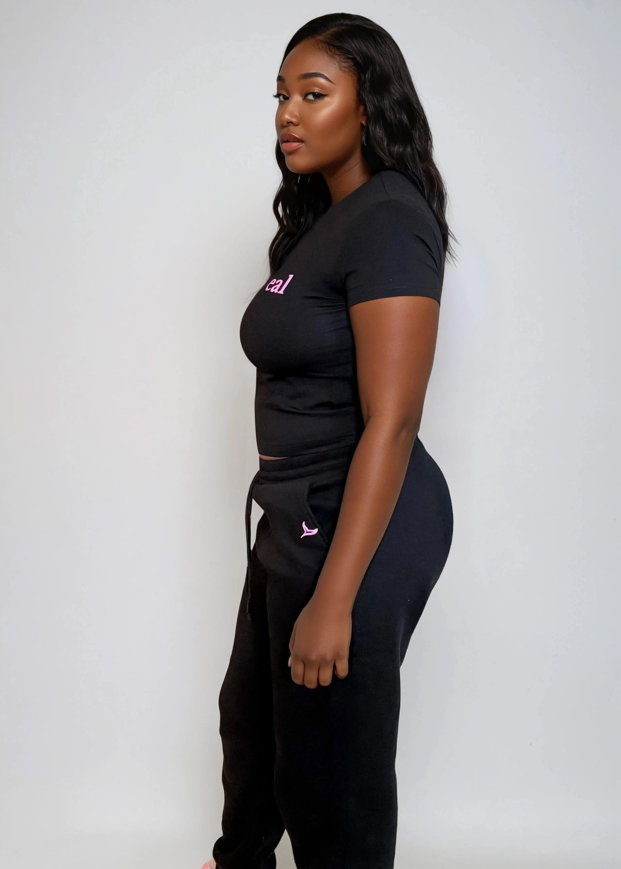 Woman wearing a black crop top & jogger pants set with 'Pink Seal' branding puff print