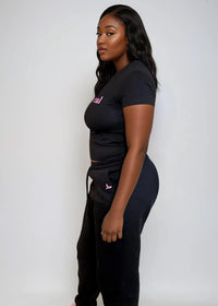 Thumbnail for Woman wearing a black crop top & jogger pants set with 'Pink Seal' branding puff print