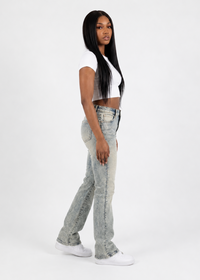 Thumbnail for A woman modeling light-wash, high-rise flared jeans with a faded, washed texture, paired with a white crop top and white sneakers, standing against a plain white studio background.