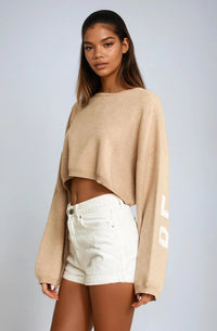 Thumbnail for Woman wearing a beige Pink Seal sweater and white shorts on a plain background
