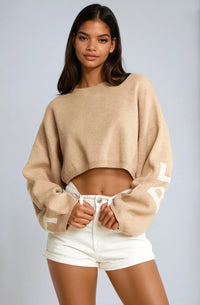 Thumbnail for Woman wearing a beige Pink Seal sweater and white shorts on a plain background