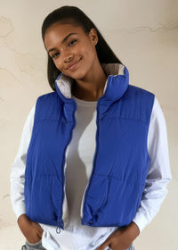Thumbnail for Woman wearing a blue puffer vest over a white shirt against a beige background