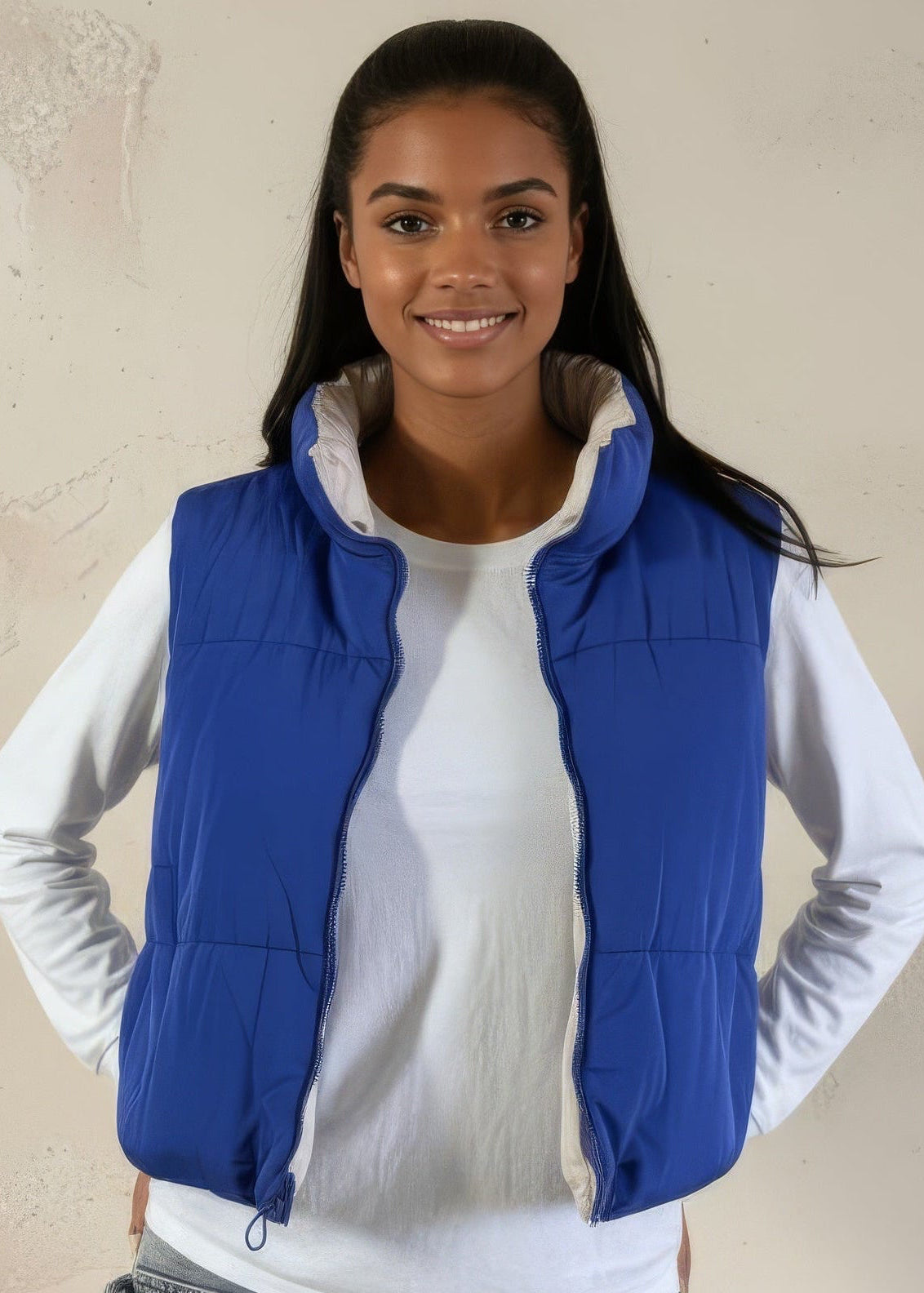 Woman wearing a blue vest over a white shirt against a beige background