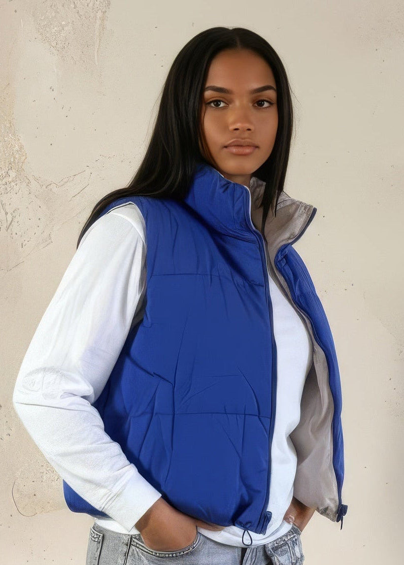 Person wearing a blue puffer vest over a white shirt with a beige background