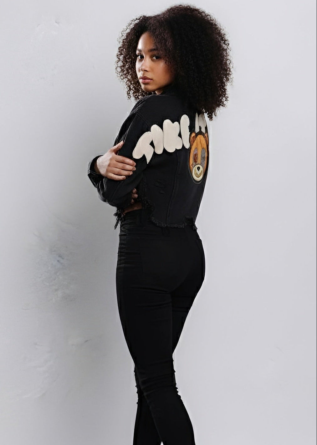 Person wearing a black cropped denim jacket with white text and graphics on a light gray background