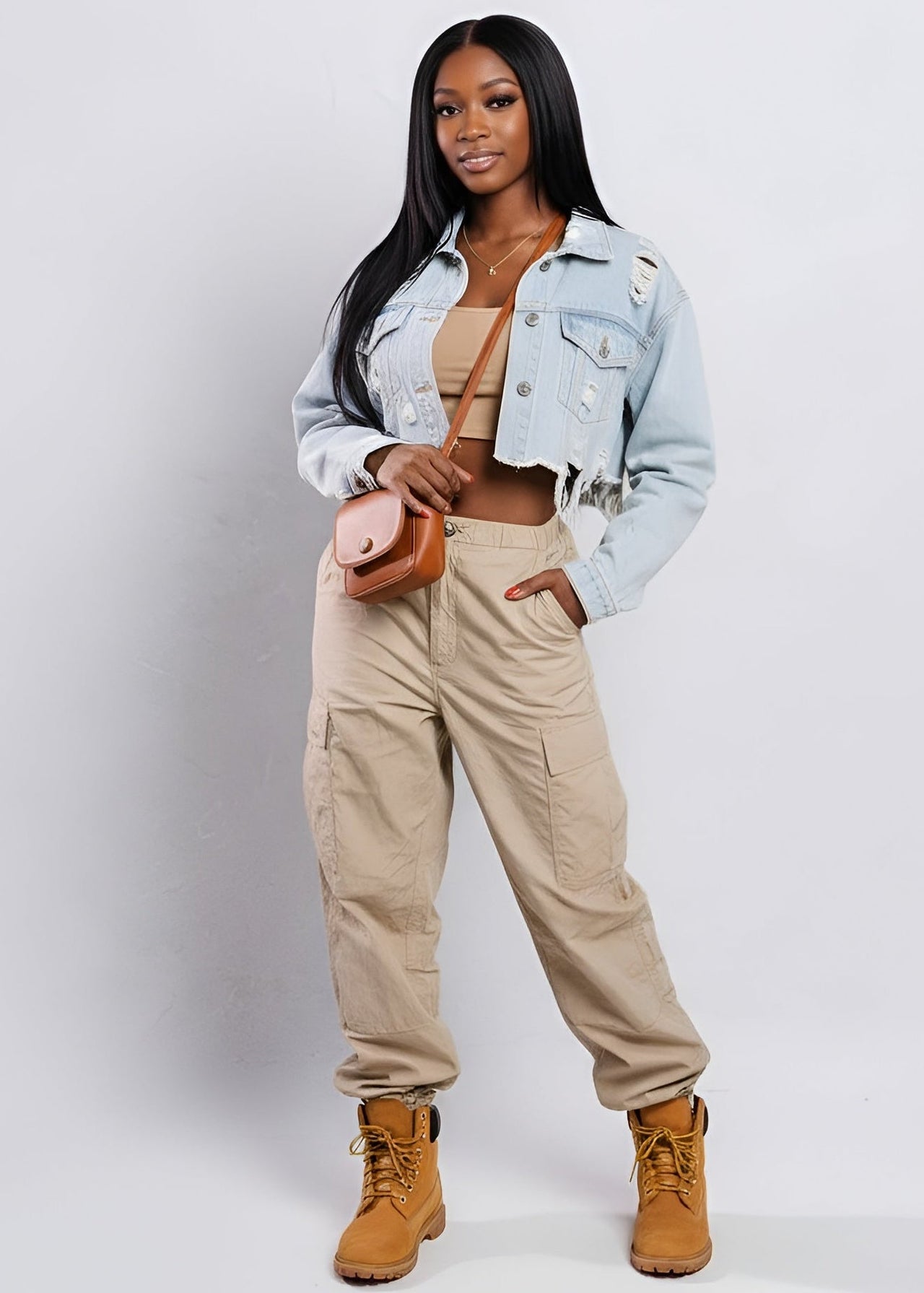 Woman wearing a Pink seal light blue denim jacket, beige pants, and brown boots on a white background