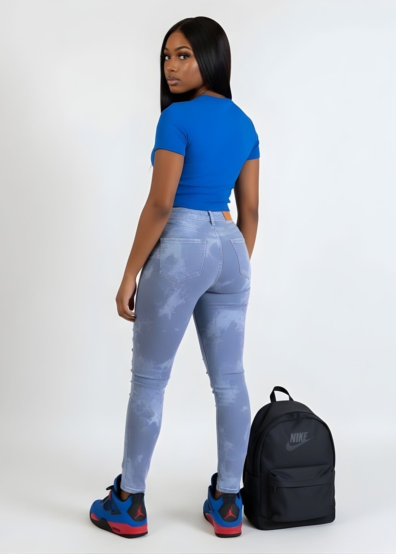 Woman wearing a pink seal blue top and light blue jeans with a black Nike backpack on a white background