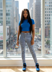 Thumbnail for Woman in blue top and Pink Seal Blue jeans standing in front of a cityscape window