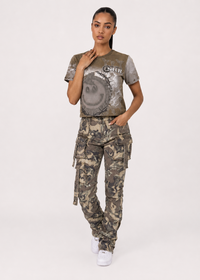 Thumbnail for A model wearing a cropped graphic t-shirt and matching camouflage cargo pants, standing against a plain light gray studio background.
