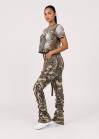 Thumbnail for A woman modeling a matching camouflage cargo pants and cropped graphic t-shirt set against a plain light gray studio background.