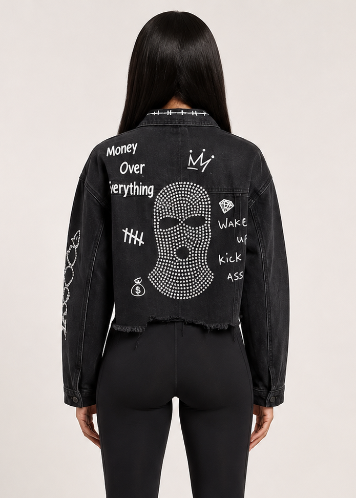 A model shown from the back wearing a black cropped denim jacket with white graphic text and a rhinestone skull design on the back, 