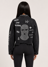 Thumbnail for A model shown from the back wearing a black cropped denim jacket with white graphic text and a rhinestone skull design on the back, 