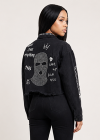 Thumbnail for A model shown from the back wearing a black frayed denim jacket with white graphic text and a rhinestone skull design on the back