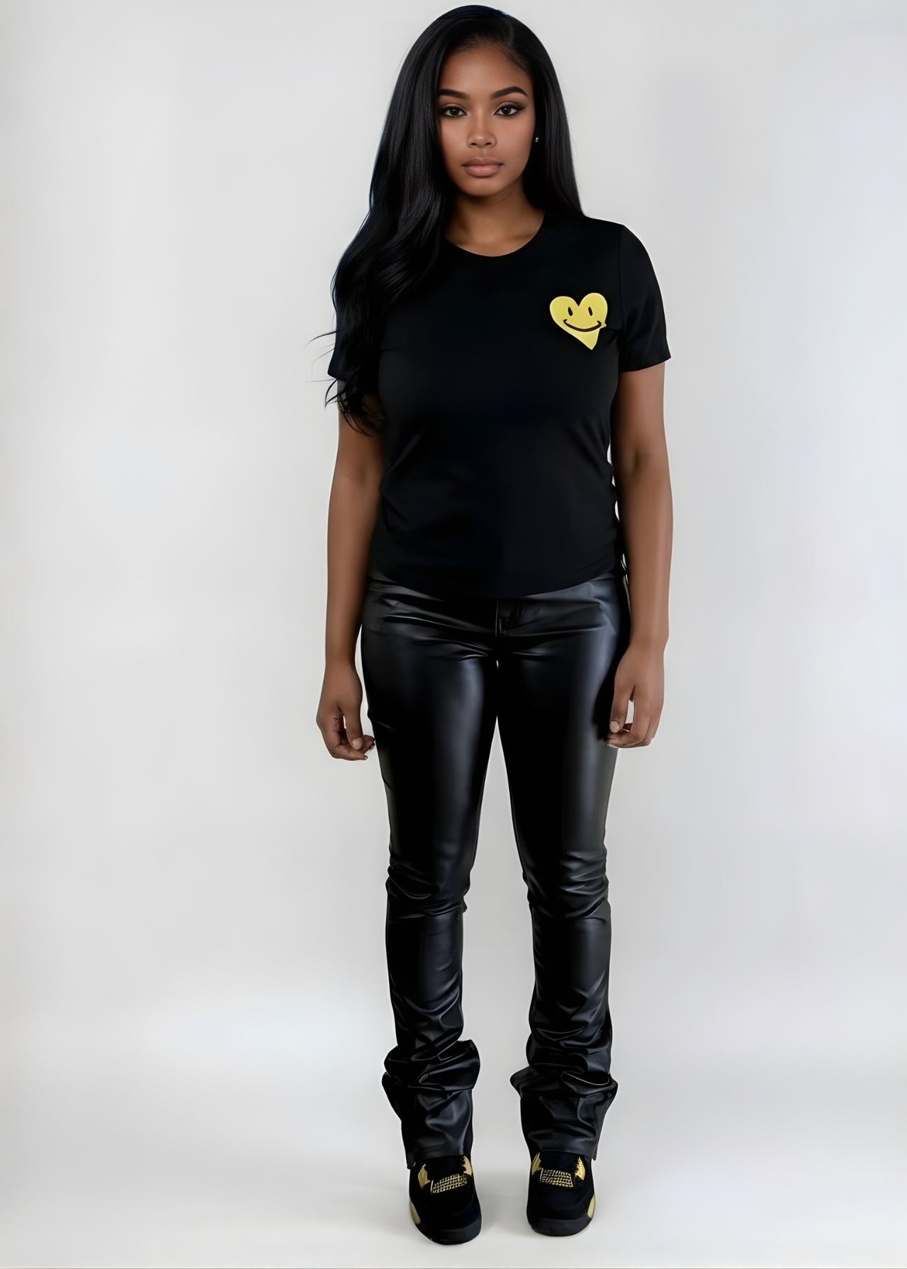 Person wearing a black t-shirt with a yellow heart design and black leather pants on a white background