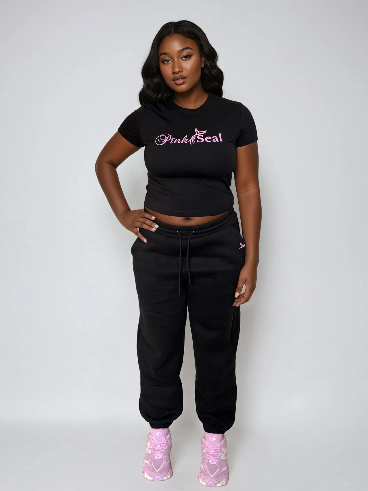 Woman wearing a black crop top and black sweatpants with 'Pink Seal' logo on a white background