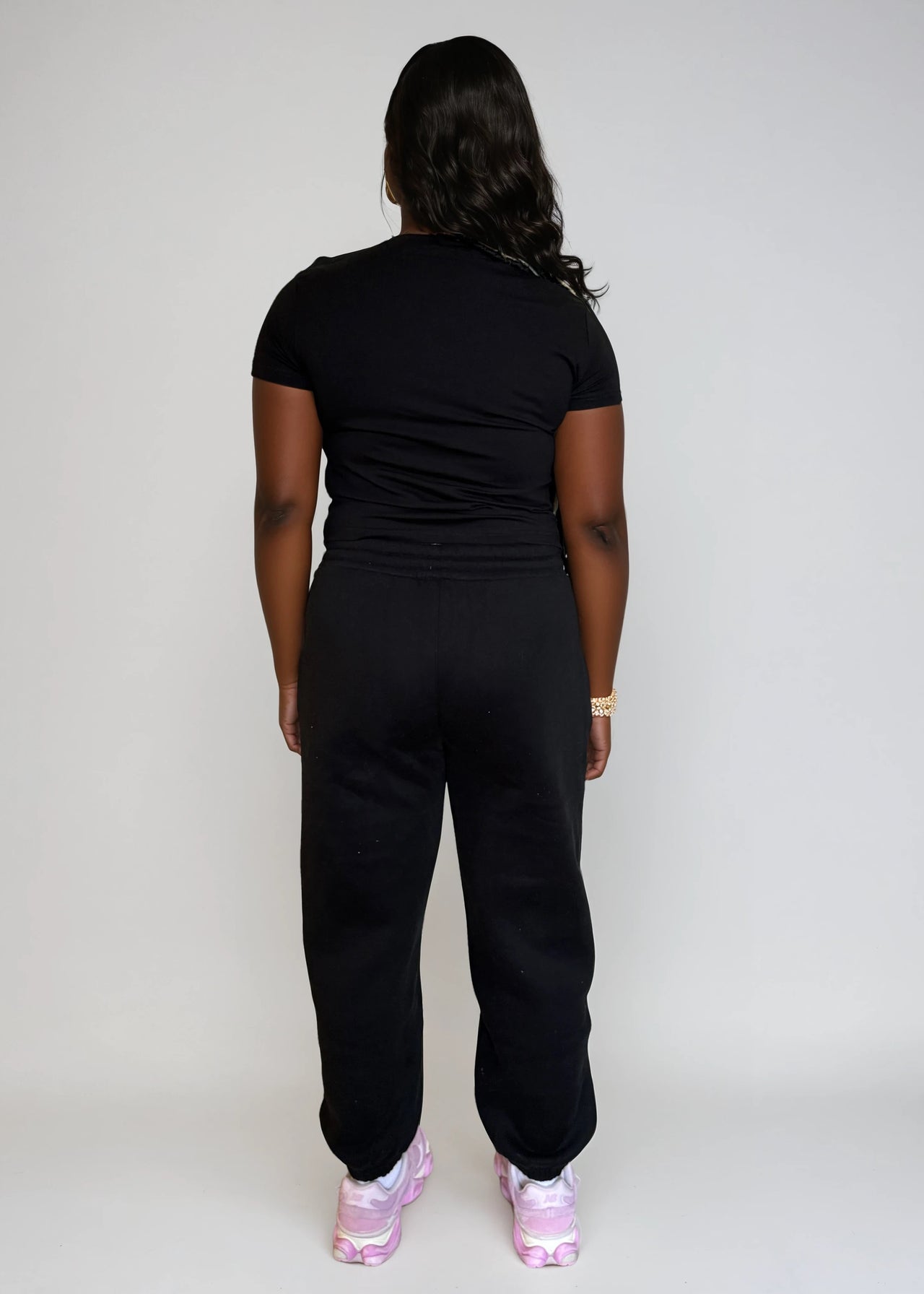Person wearing a black outfit with pink shoes on a plain background