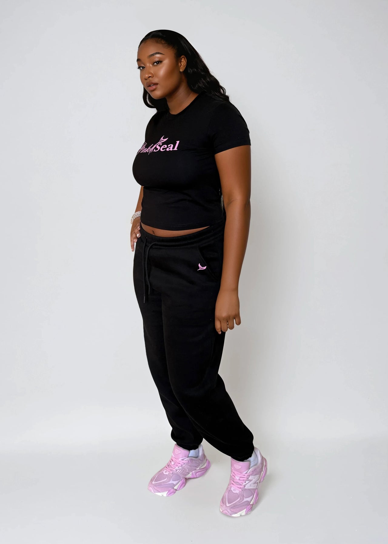 Person wearing a black outfit with pink text and pink sneakers on a white background