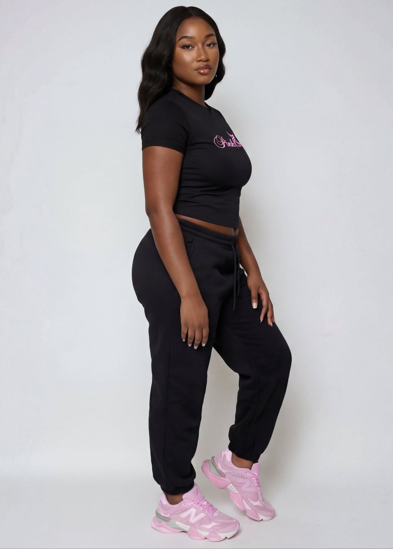 Woman wearing a Pink Seal branded black outfit with pink shoes on a white background