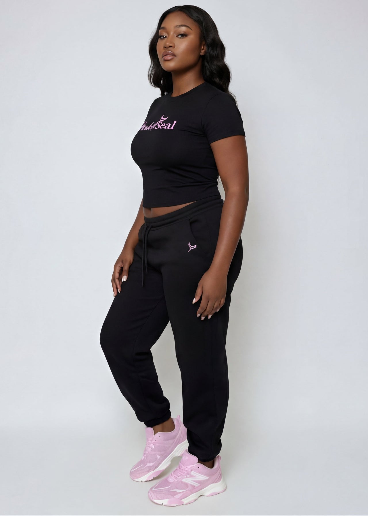 Woman wearing a Pink Seal branded black outfit with pink shoes on a white background