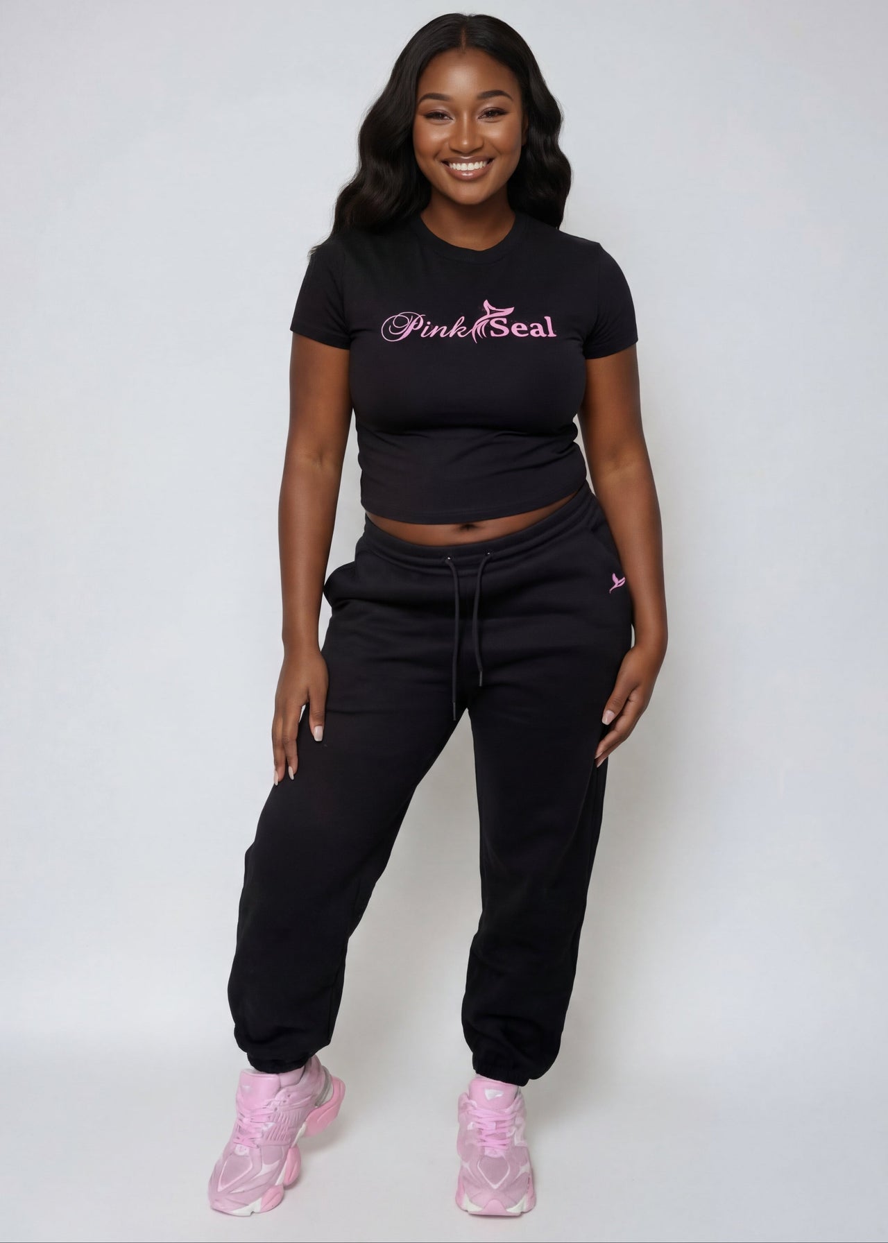Woman wearing a Pink Seal branded black outfit with pink shoes on a white background