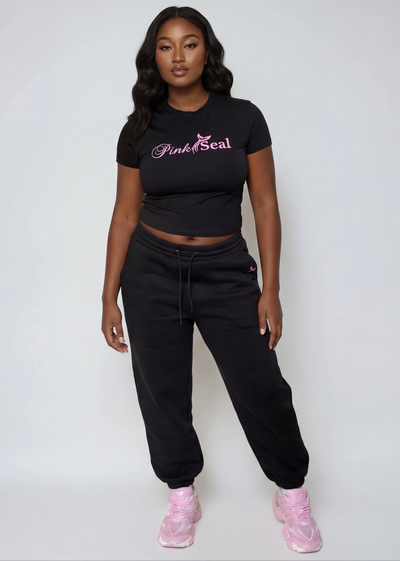 Woman wearing a Pink Seal branded black outfit with pink shoes on a white background