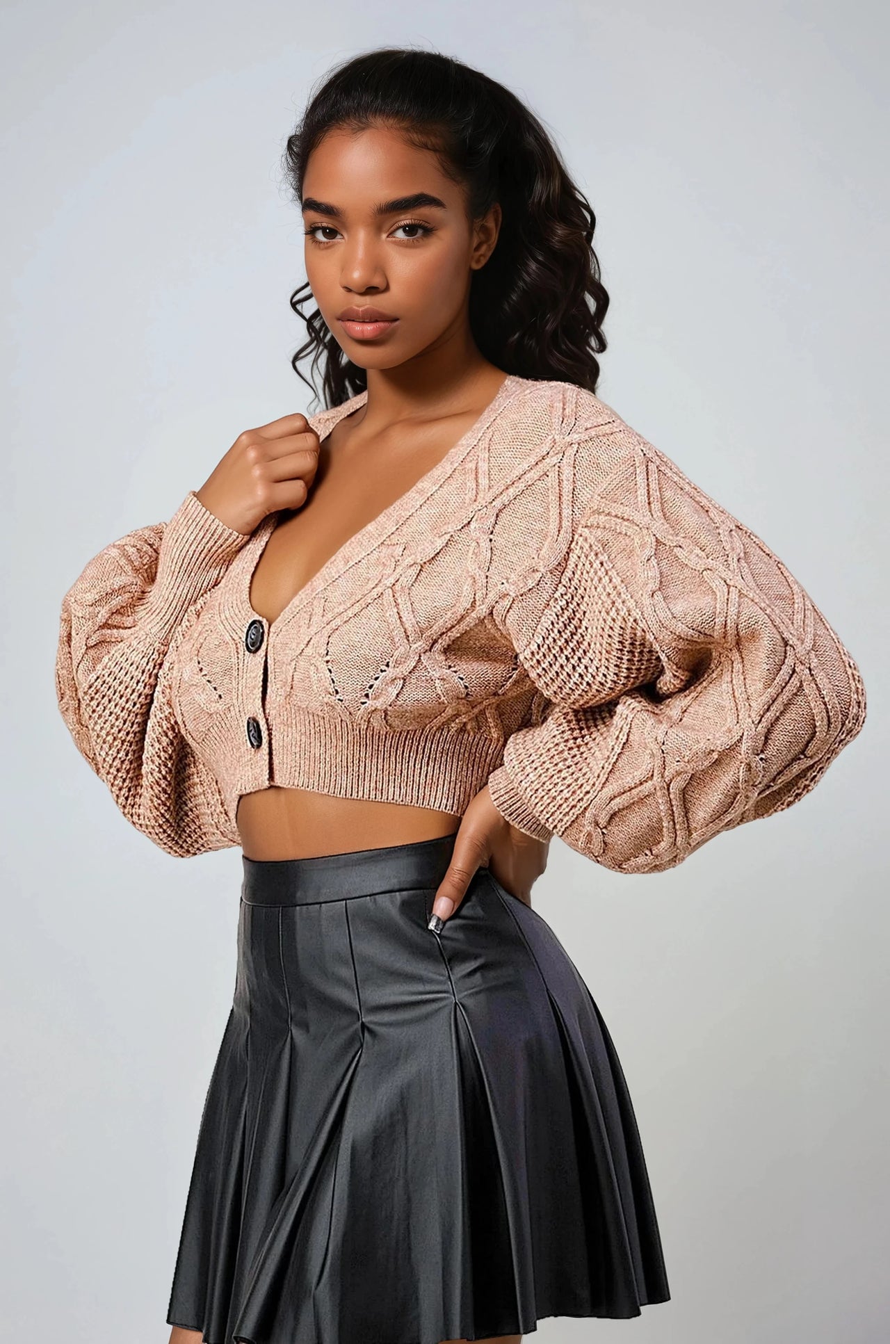 Pink Seal Snuggle Crop beige cable knit cardigan and black pleated skirt on a light gray background