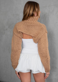 Thumbnail for Woman wearing a beige knitted cardigan over a white top and shorts against a gray background
