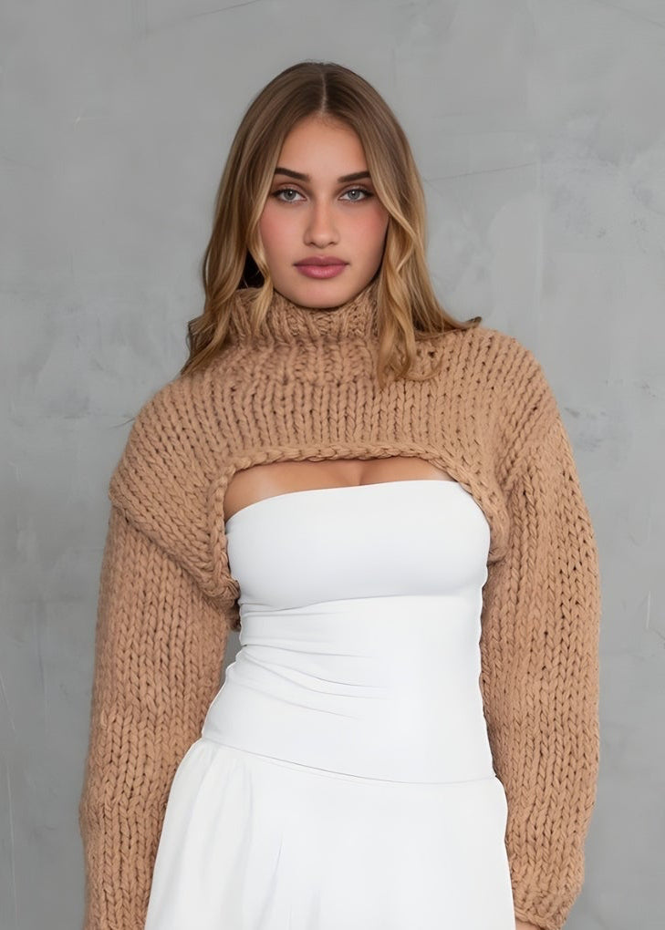 Woman wearing a beige sweater over a white top and skirt against a gray background