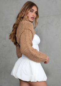 Thumbnail for Woman wearing a brown knitted sweater over a white top and skirt against a gray background