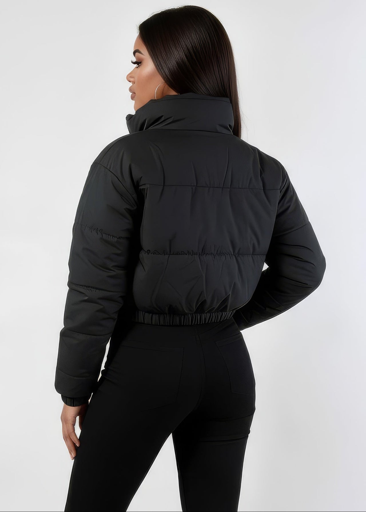 Person wearing a black puffer winter down jacket and pants on a white background
