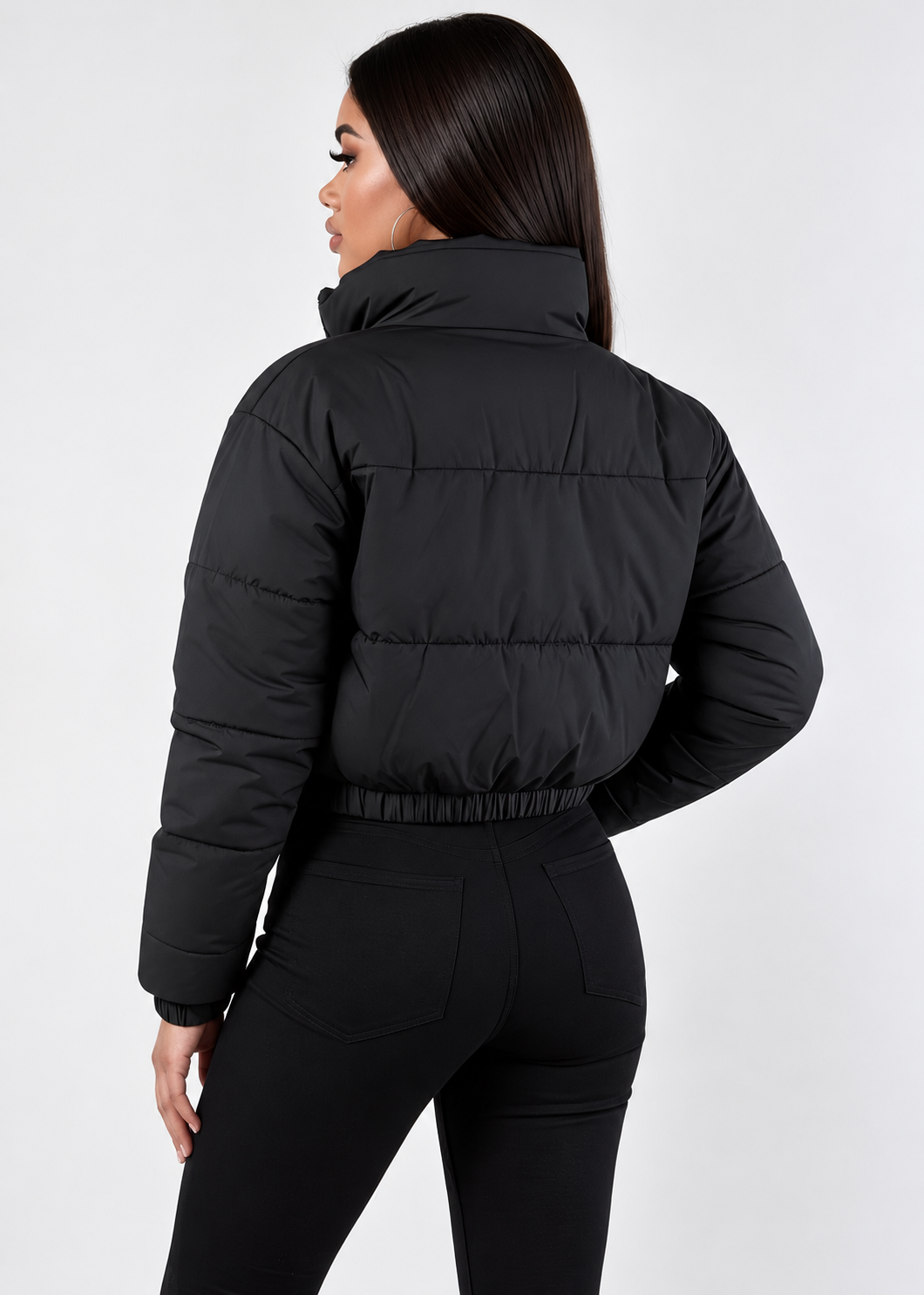 A woman shown from the back wearing a black cropped puffer jacket with horizontal quilting and a high collar, paired with black leggings, against a light gray studio background.