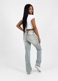 Thumbnail for A woman with long black hair is shown from the back wearing light-wash, high-rise flare jeans, a white crop top, and white sneakers against a plain white studio background.