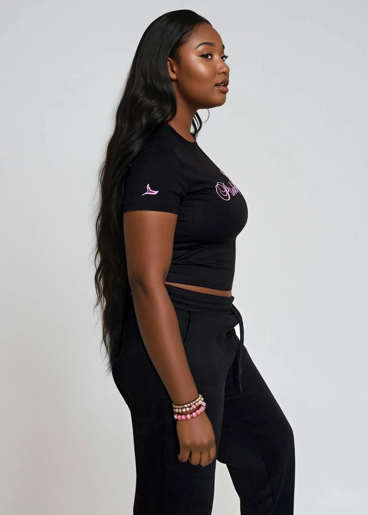 Woman wearing a black crop top & jogger pants set with 'Pink Seal' branding puff print