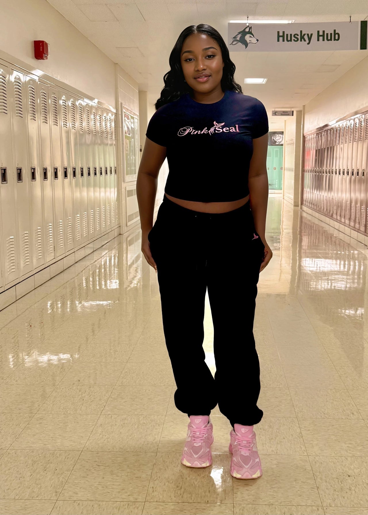 Woman wearing a black crop top & jogger pants set with 'Pink Seal' branding puff print